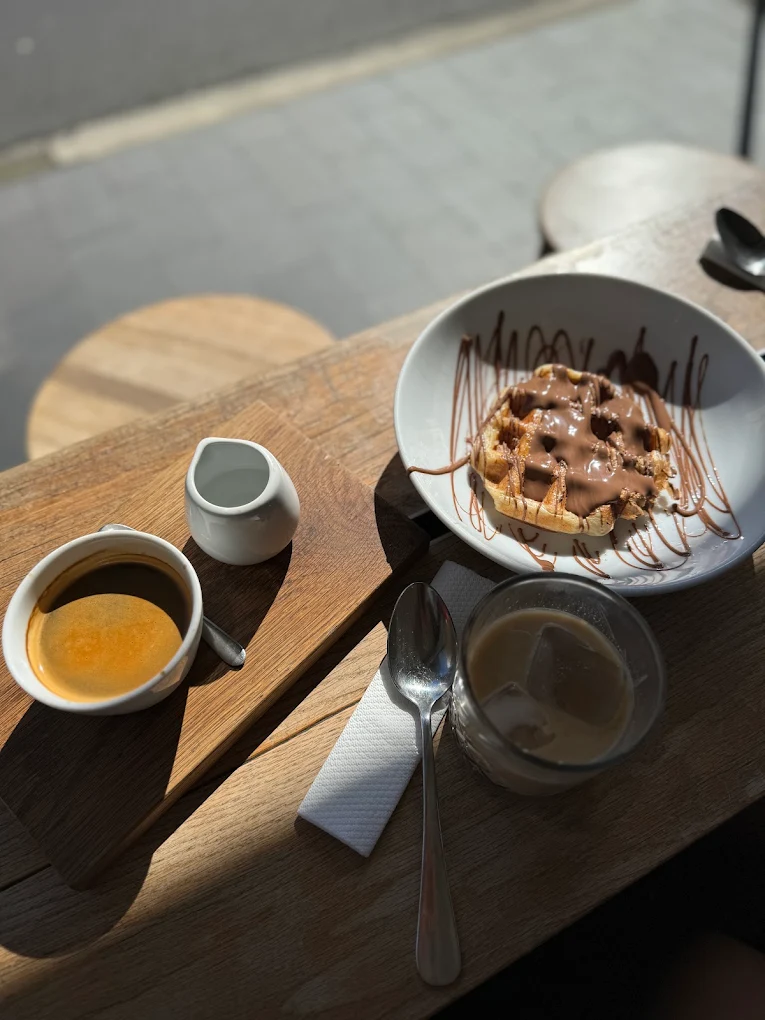 Belgian chocolate waffle and iced latte on a timber table in morning sun